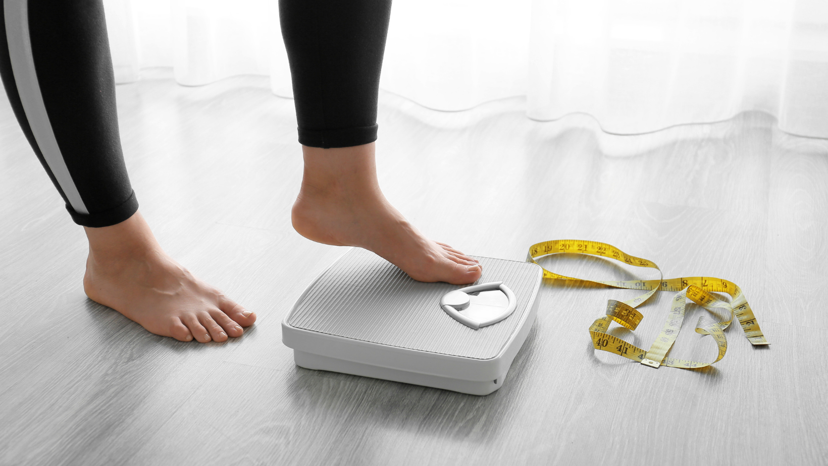 person stepping on scale with yellow measuring tape on the floor